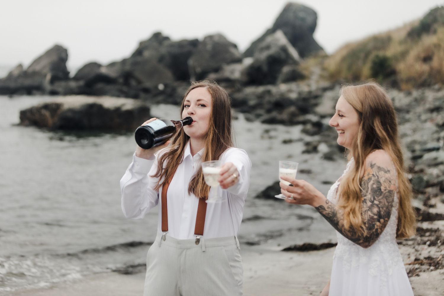 Bride offers a glass of champagne to the elopement photographer while her new wife smiles