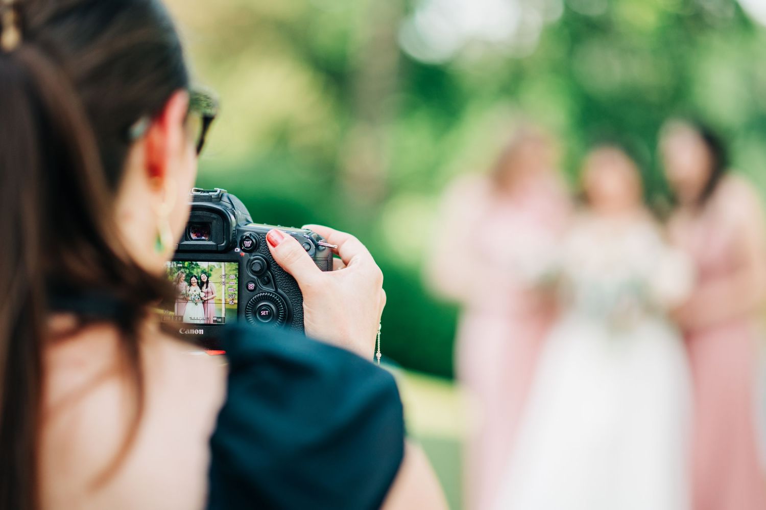 Photographer capturing bridesmaids in pink dresses and bride holding bouquet at outdoor wedding ceremony.