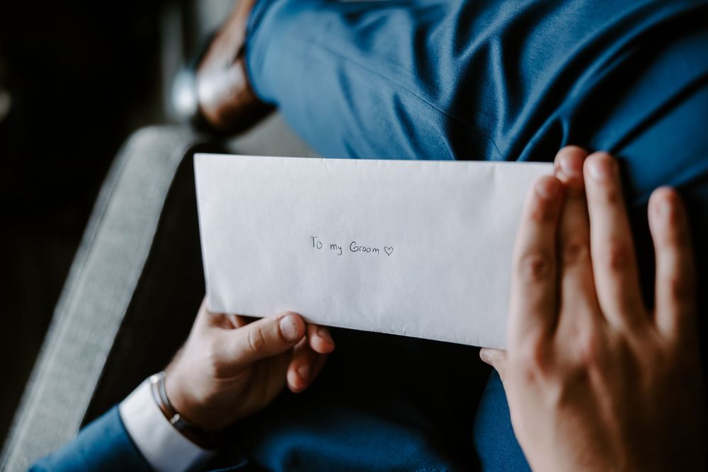 Groom in blue suit holding a white envelope addressed to his bride on wedding day.