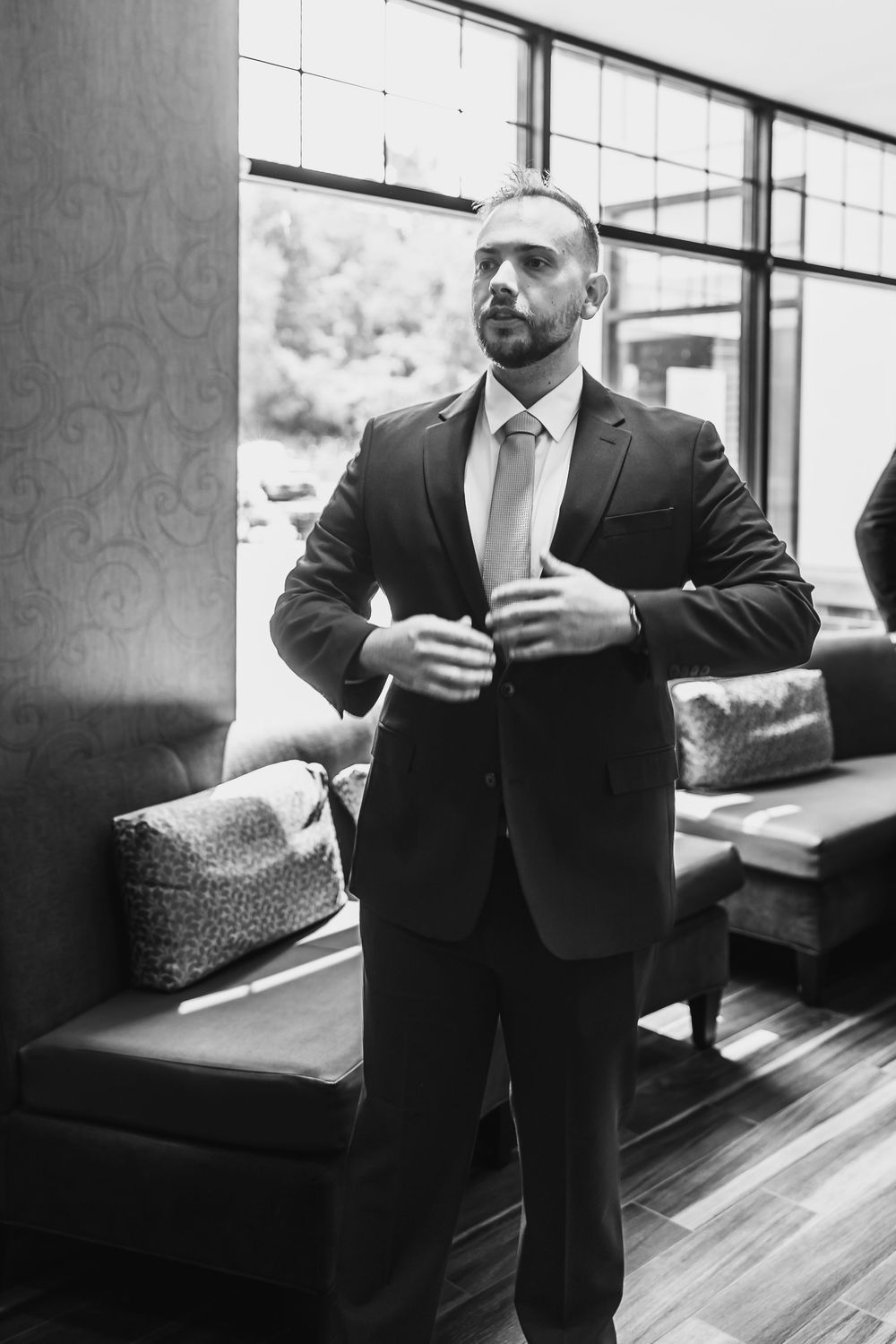 Confident groom in black suit and tie adjusting his jacket in a stylish black and white portrait.