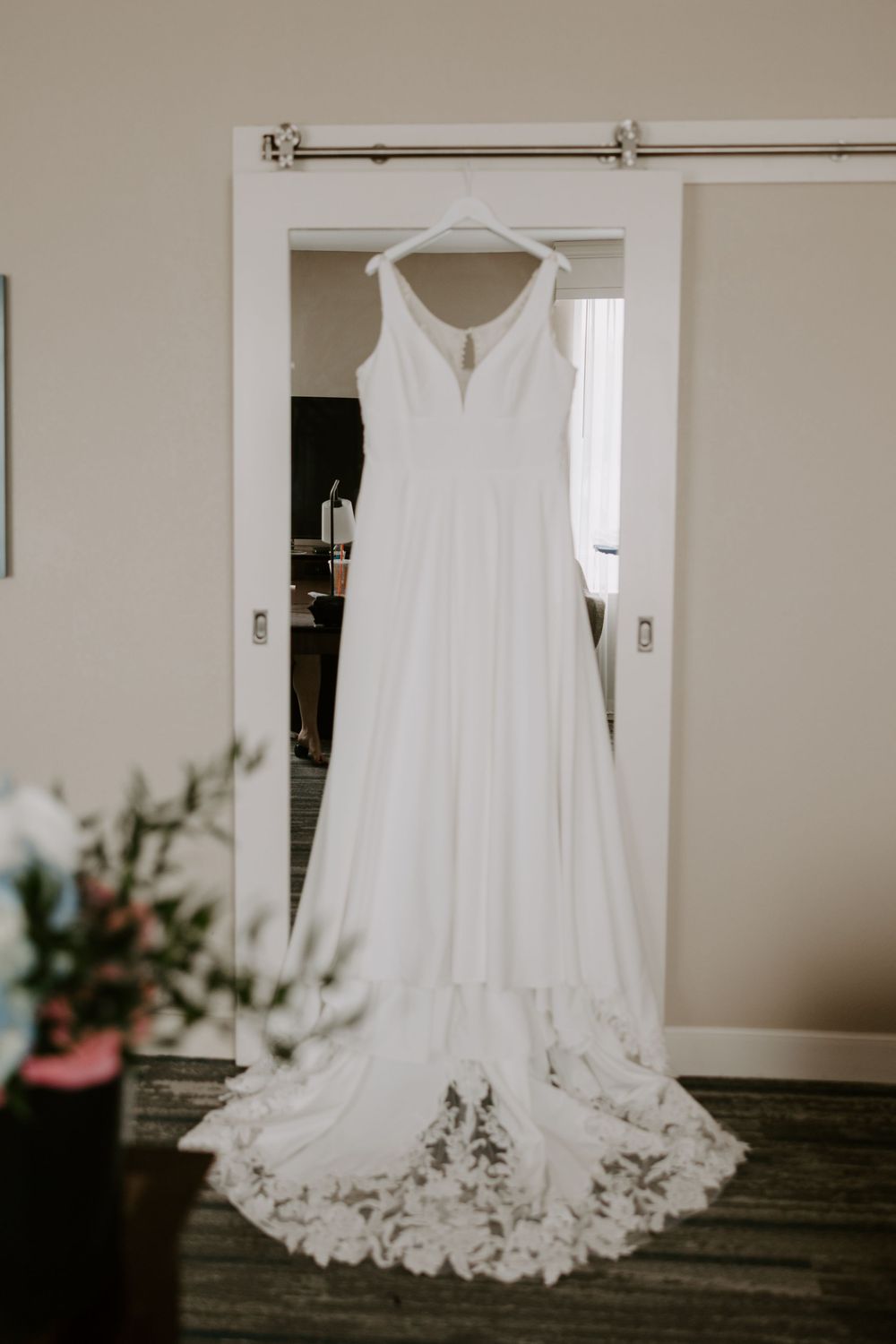 Elegant white A-line wedding dress with lace trim train hanging on a barn door before the ceremony.