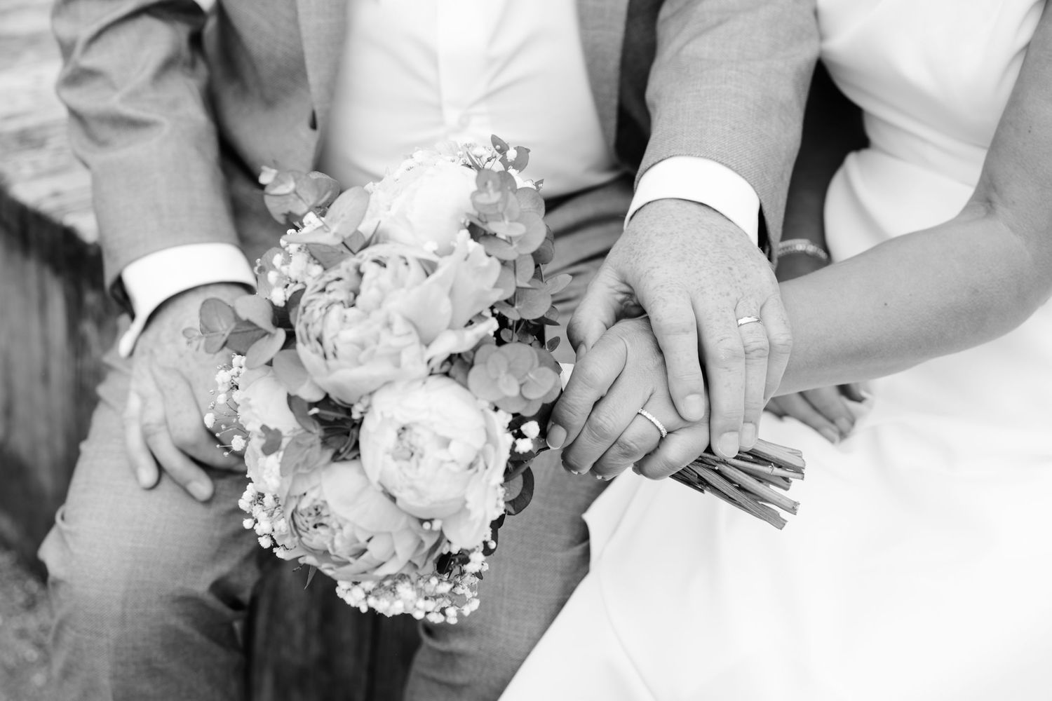 Two wedding rings nestled in a white rose bouquet, featuring a diamond engagement ring and a silver band.