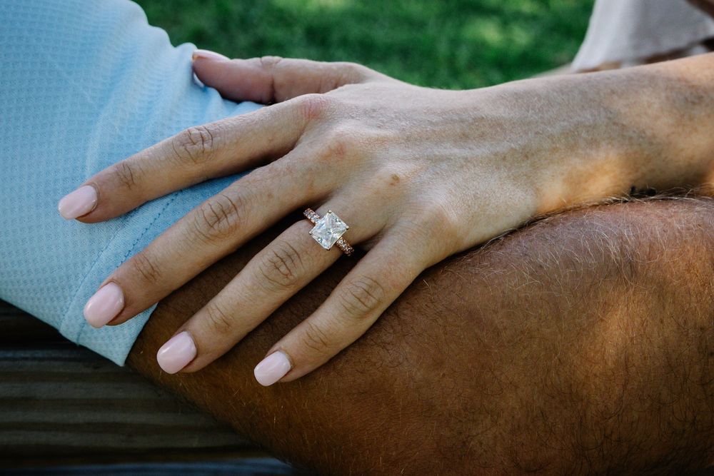 Close-up of a woman's hand displaying a stunning emerald-cut diamond engagement ring on a rose gold band.