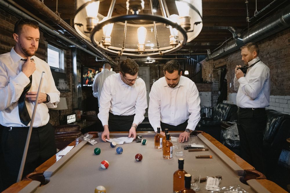 Groomsmen in white shirts playing pool at a rustic bar venue before a wedding ceremony.