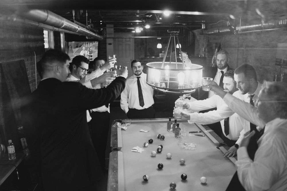 Group of men in dress shirts toasting with glasses around a pool table in a vintage black and white photo.