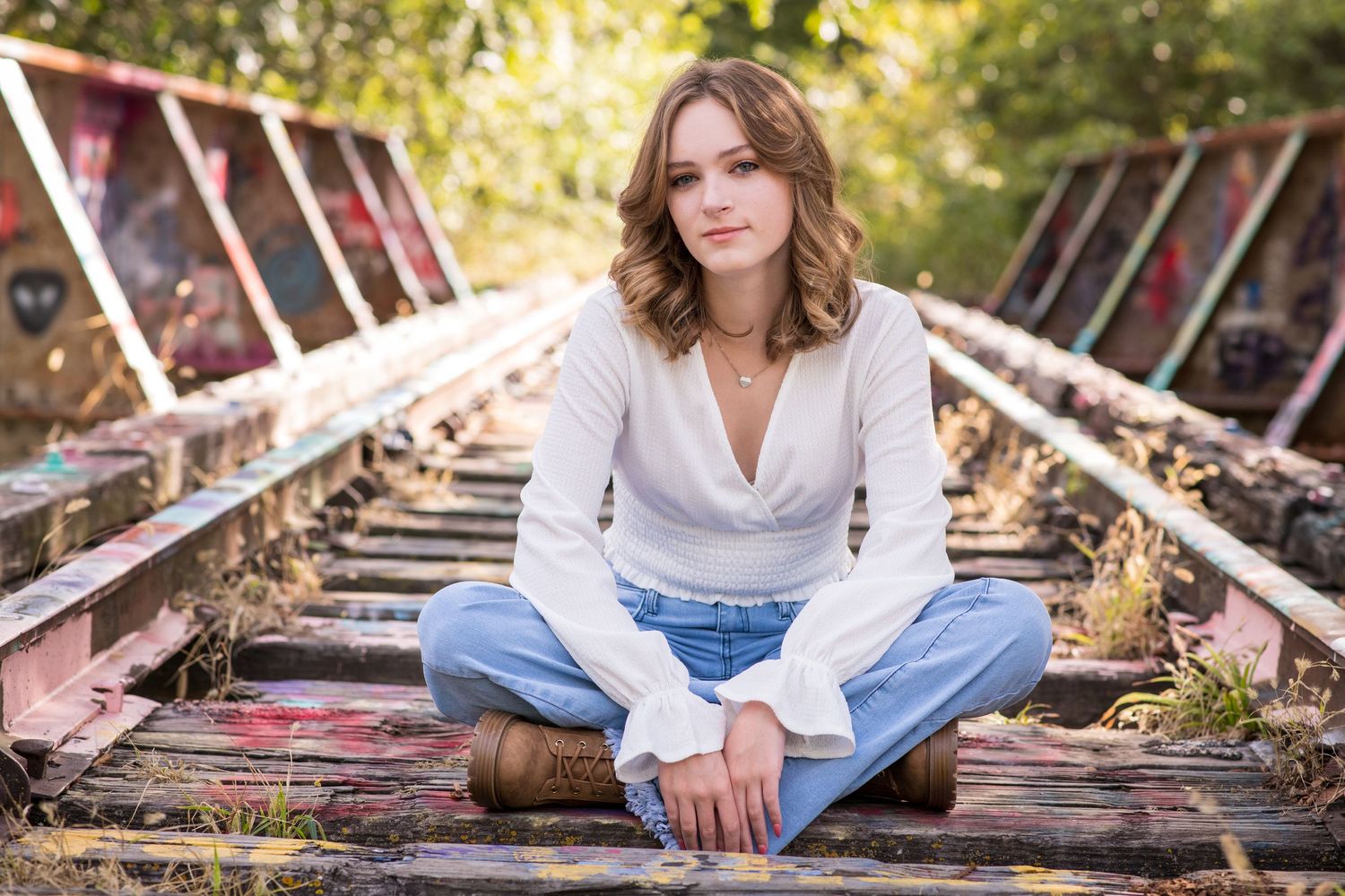 Young woman in white blouse and jeans sitting cross-legged on old railroad tracks.