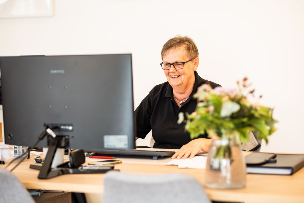 Smiling professional man with glasses working at a desk with computer monitor and fresh flowers in bright office.