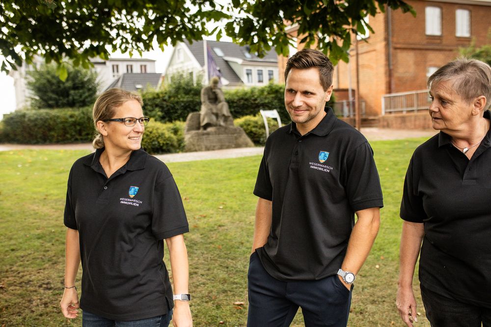 Three colleagues in matching black polo shirts walking and laughing together outdoors near a brick building.