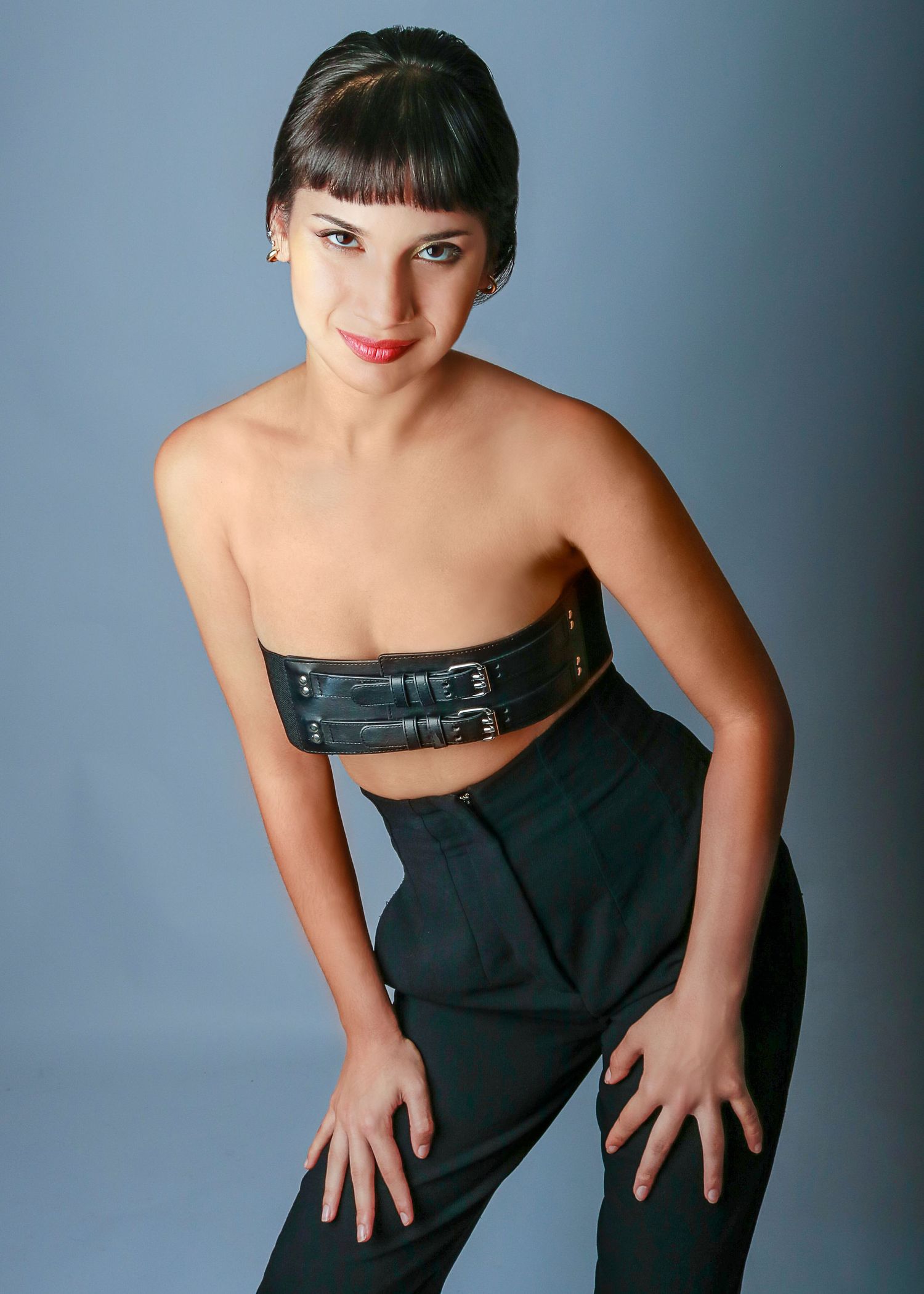 Young woman in black strapless corset top and trousers posing against gray studio background.