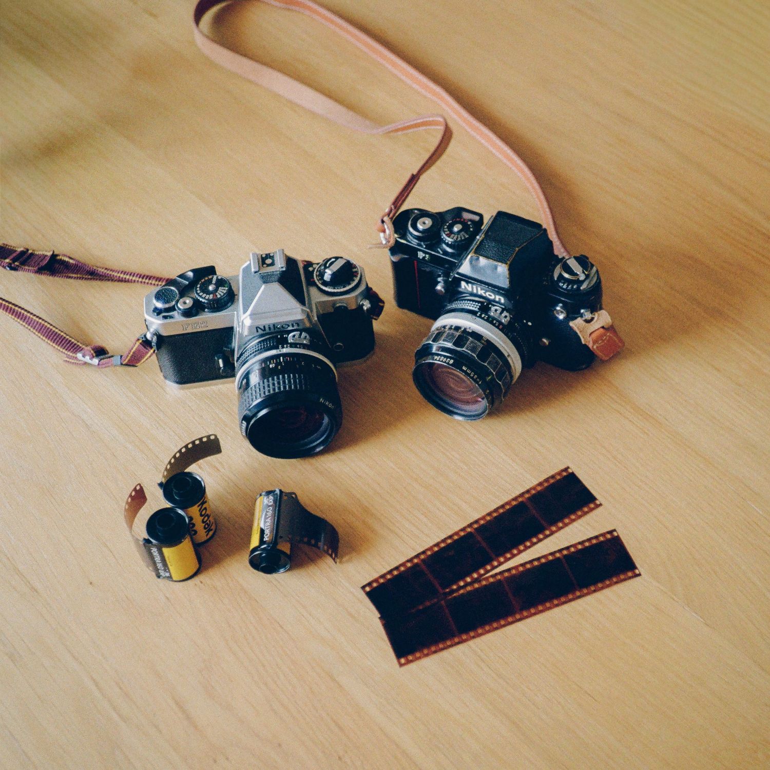 Two vintage film cameras with leather straps alongside Kodak film rolls and developed film strips on a wooden surface.