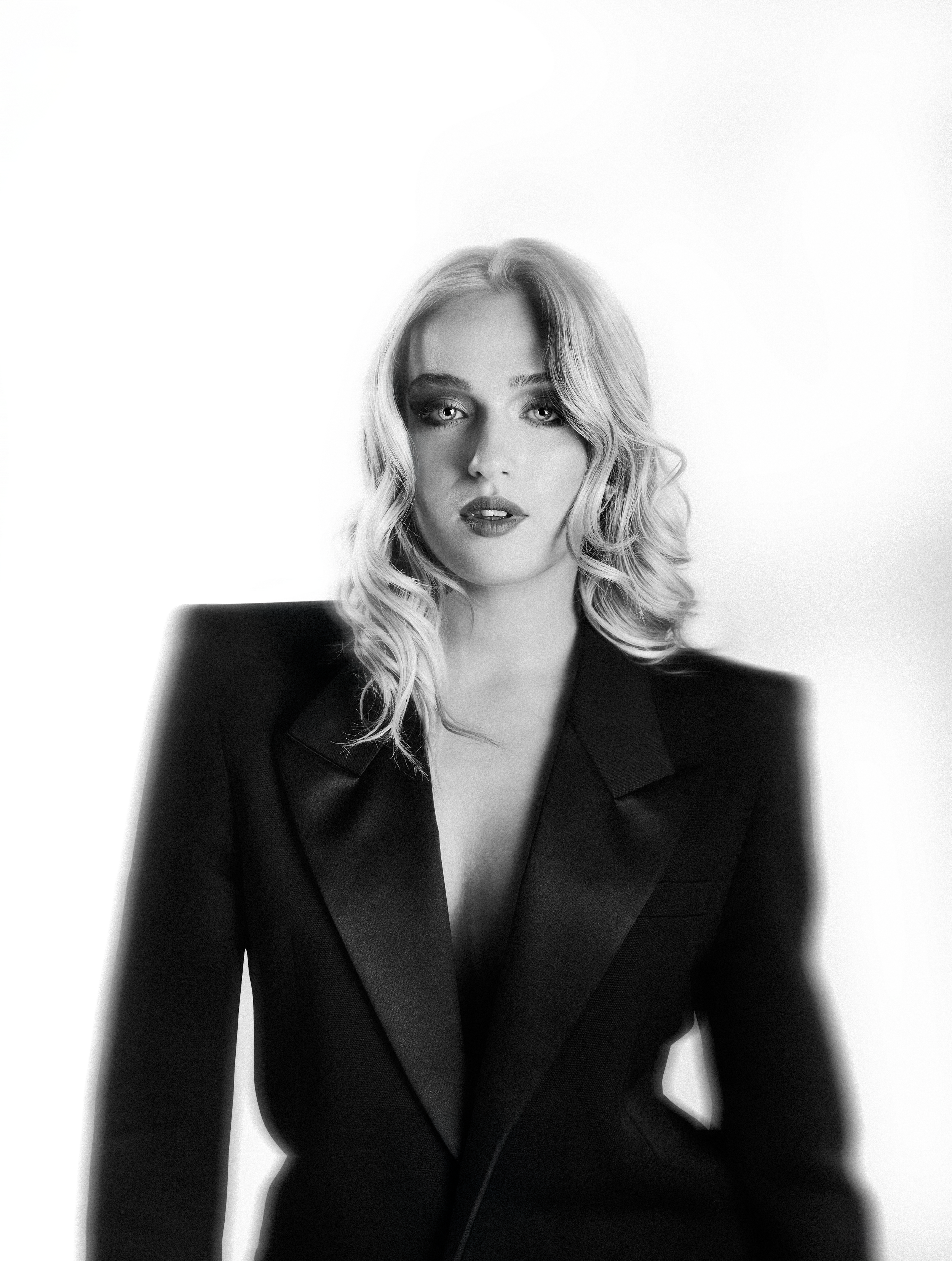 Black and white portrait of a blonde woman in a black blazer, posing confidently against a white background.