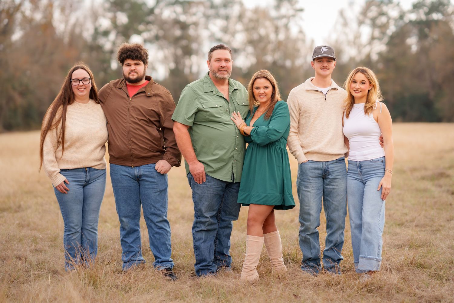 Family of six posing together in an open field during autumn, wearing casual attire and smiling at the camera.