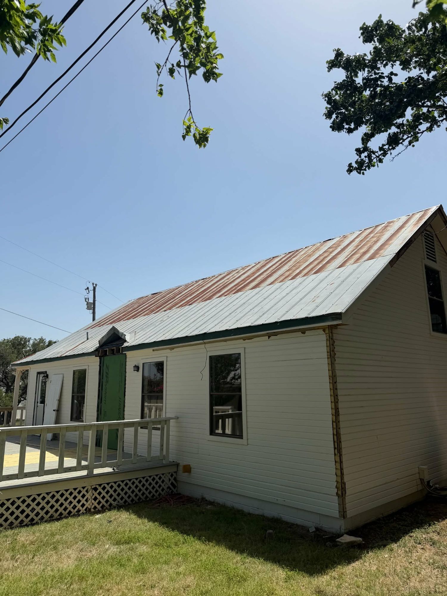 Worker stands on roof deck during residential roofing replacement project with scaffolding and exposed wood sheathing on sunny day.