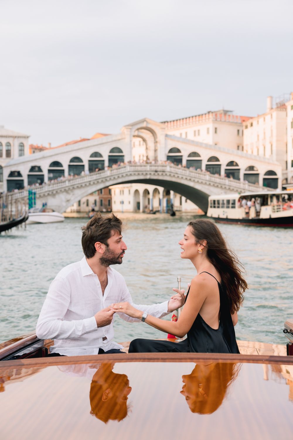 Couple holding hands on a boat with the Rialto Bridge in Venice, Italy in the background.
