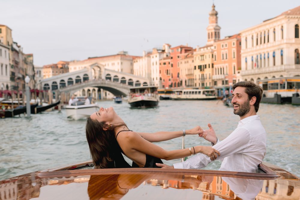 Romantic couple holding hands on a boat along the Grand Canal with the Rialto Bridge in Venice, Italy.