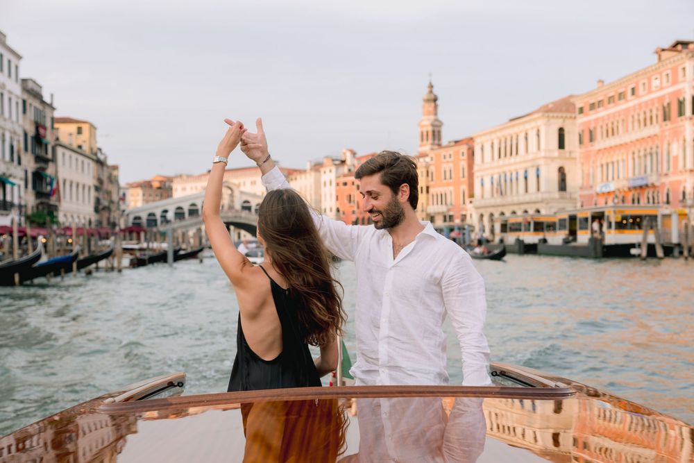 Couple dancing on a gondola boat with Venice Grand Canal and Rialto Bridge in the background.