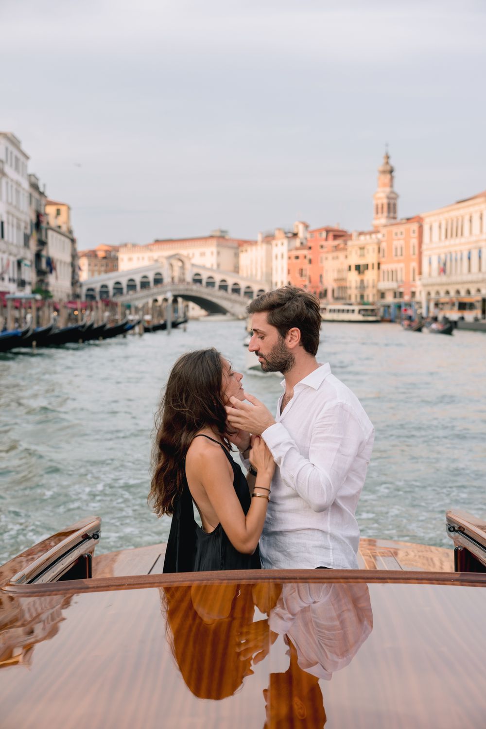 Couple sharing a romantic moment on a boat on the Grand Canal in Venice, Italy, with the Rialto Bridge behind.
