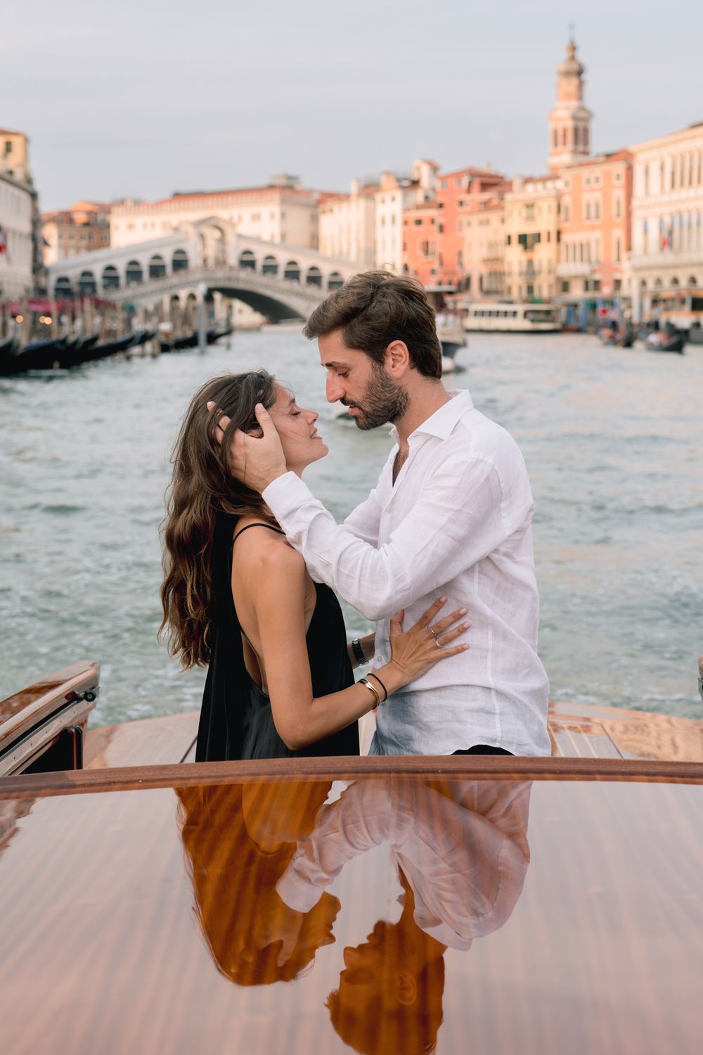 Romantic couple embracing on a boat in Venice's Grand Canal with the iconic Rialto Bridge in the background.
