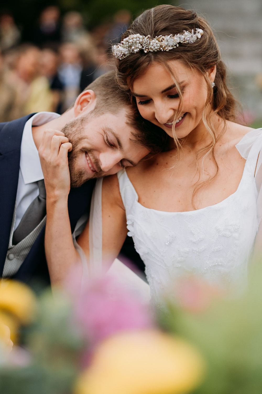 Bride wearing floral crown tenderly embraces smiling groom during wedding ceremony.