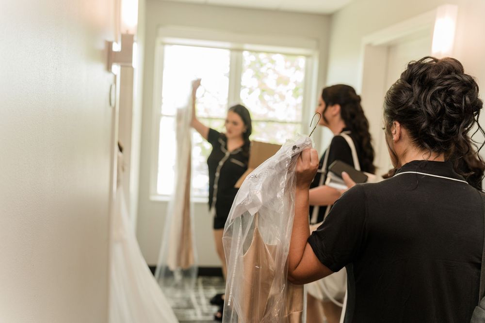Bridesmaids helping prepare a wedding dress in a bright dressing room before the ceremony.