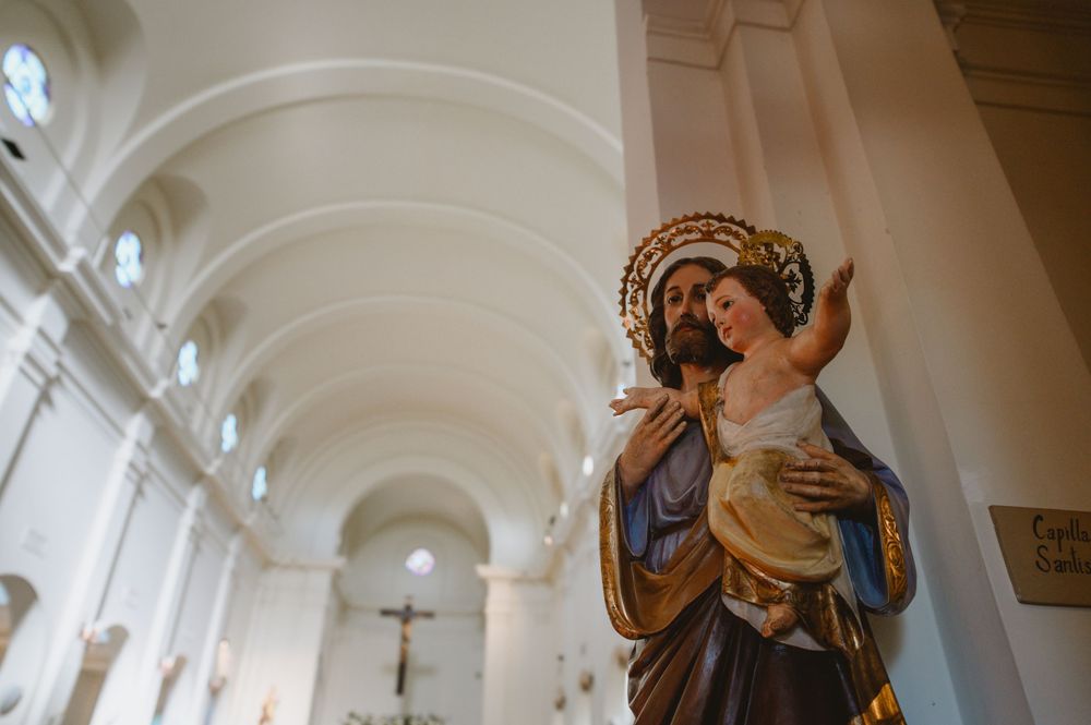 Religious statue of Saint Joseph holding baby Jesus in white Catholic church interior.
