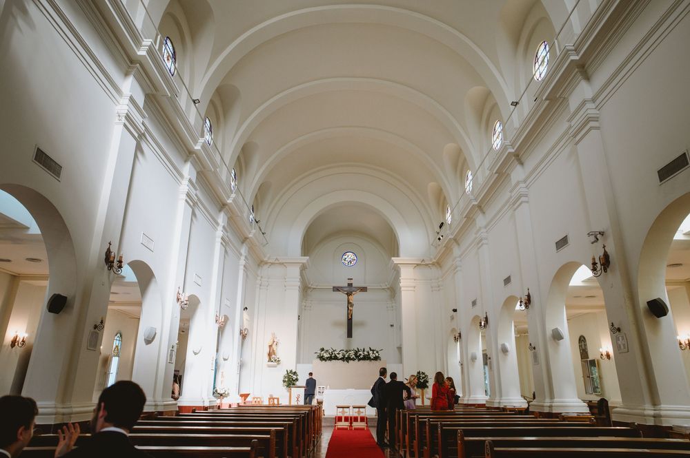 Elegant white Catholic church interior with wooden pews and crucifix during wedding ceremony.
