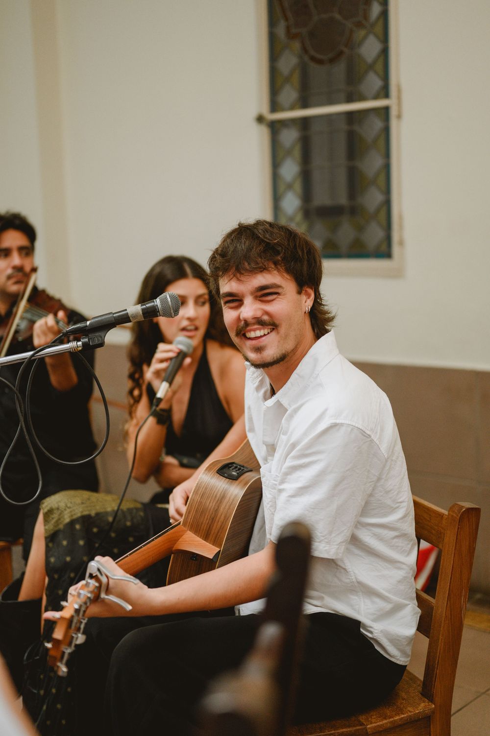 Smiling guitarist in white shirt performing with band at wedding ceremony in church.