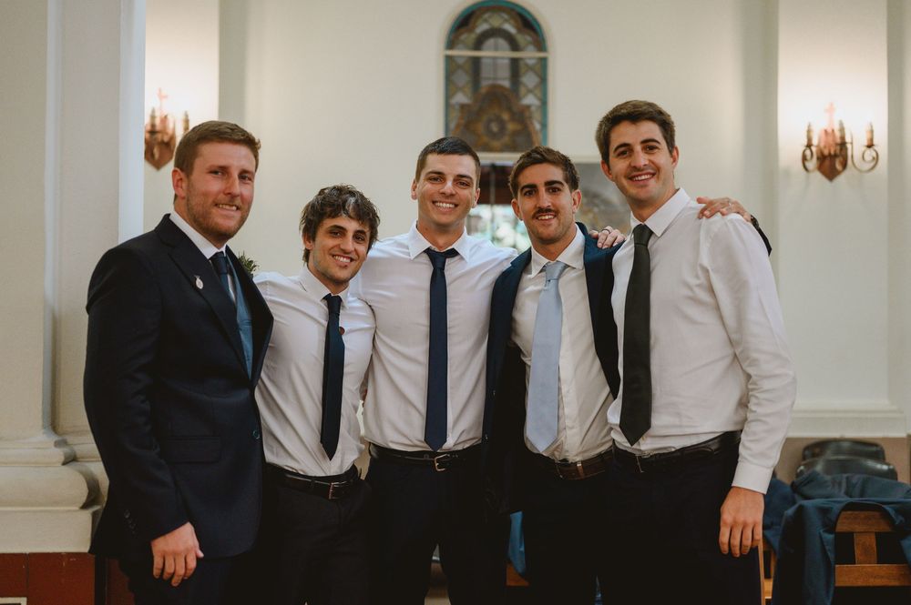 Five young men in suits and ties posing together inside church at wedding.