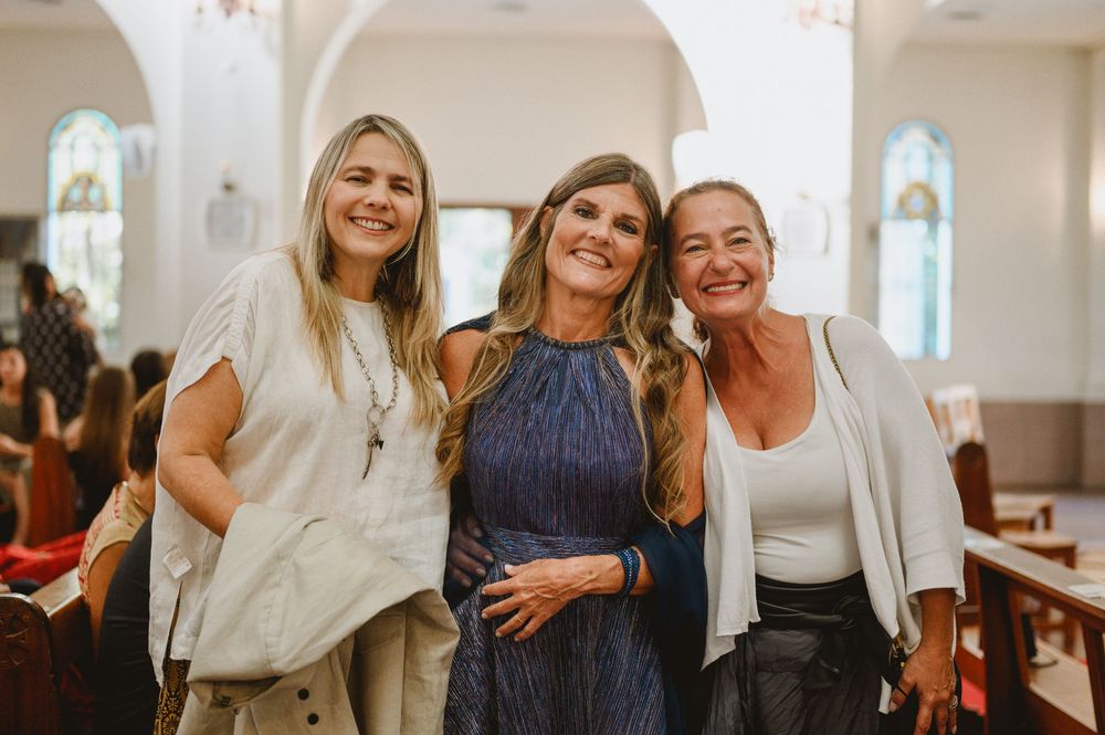 Three smiling women posing together inside church at wedding celebration event.