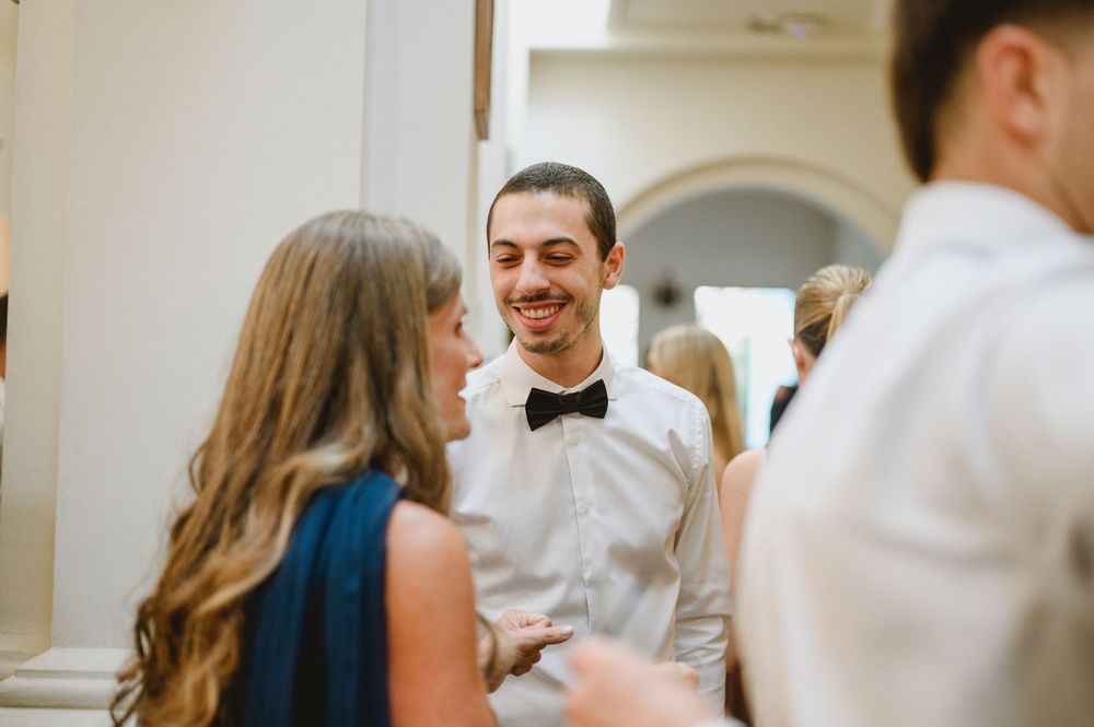 Man in white shirt and black bow tie smiling while conversing at a wedding reception.