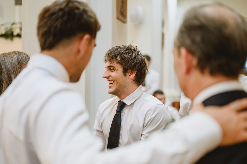 Young man in white shirt and black tie laughing with guests at a wedding celebration.