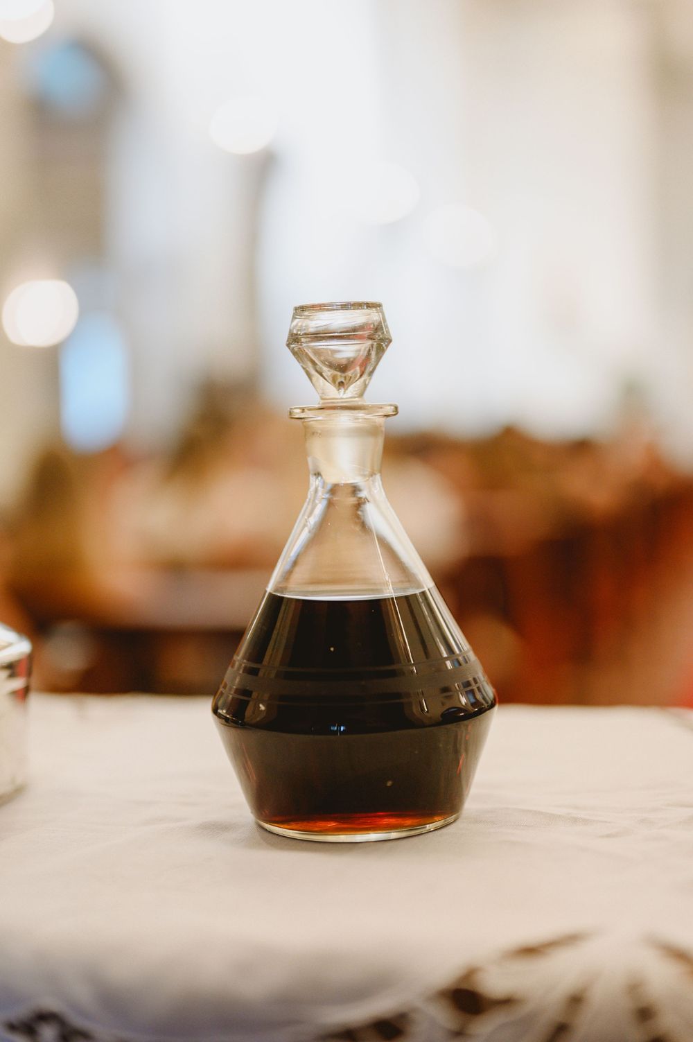 Elegant glass decanter filled with dark liquid placed on white tablecloth at wedding reception.