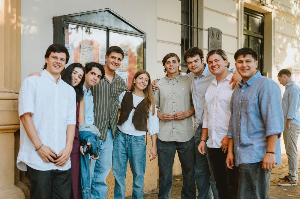Group of nine young adults smiling together outside a building at a wedding celebration.