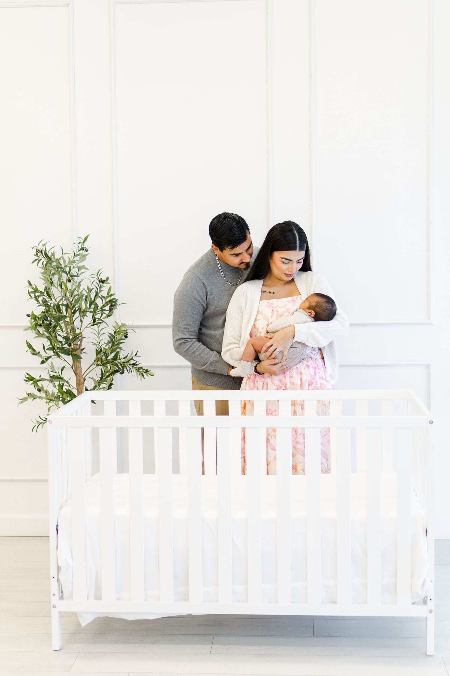 Light and airy studio newborn session with a mom cradling her newborn baby and dad cuddling behind her, smiling down at their baby