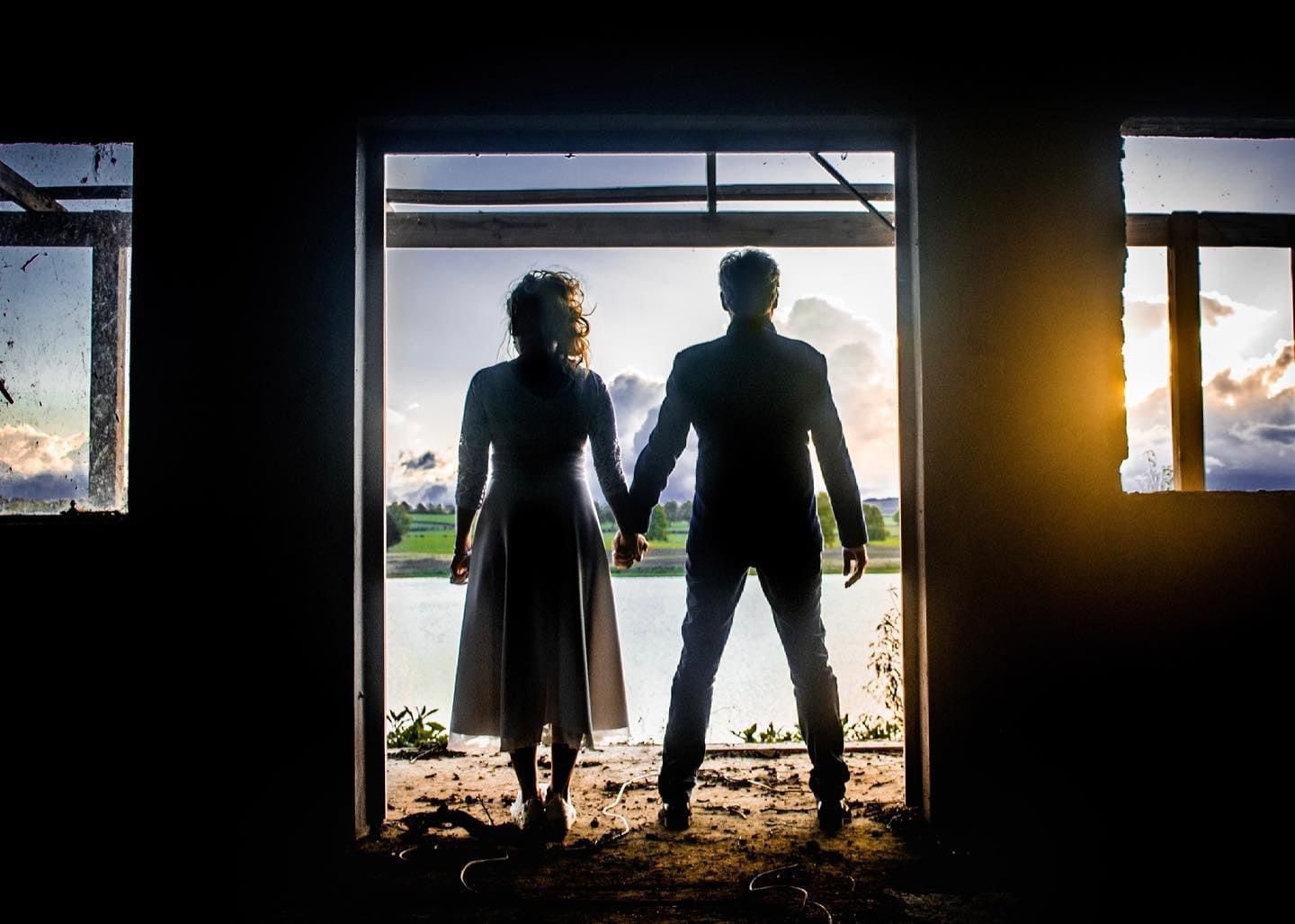 Silhouette of a newly-wed couple holding hands in a doorway of an abandoned building at golden sunset.