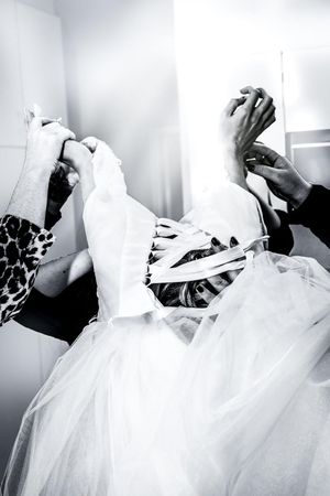 Black and white photo of hands helping a bride lace up her wedding dress corset back.