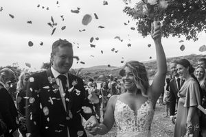 Black and white photo of a joyful newlywed couple walking through confetti shower after their wedding ceremony.