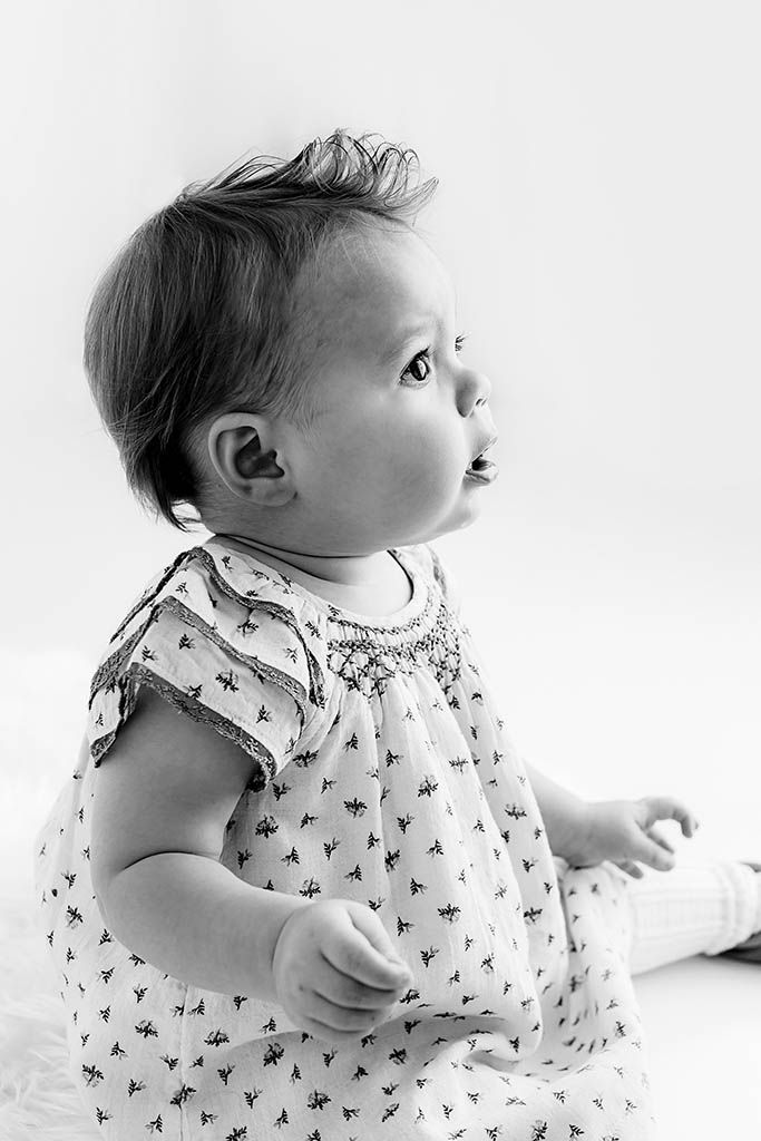 Black and white portrait of a cute baby in a floral dress, looking up with curiosity.