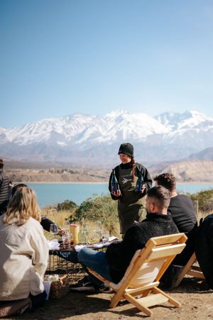 Outdoor wine tasting event with guests seated near turquoise lake and snow-capped mountains.