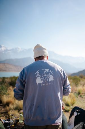 Man in Chirivia sweatshirt and beanie gazing at mountain lake landscape outdoors.