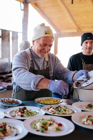 Smiling chef in beanie and apron plating gourmet dishes at an outdoor culinary event.