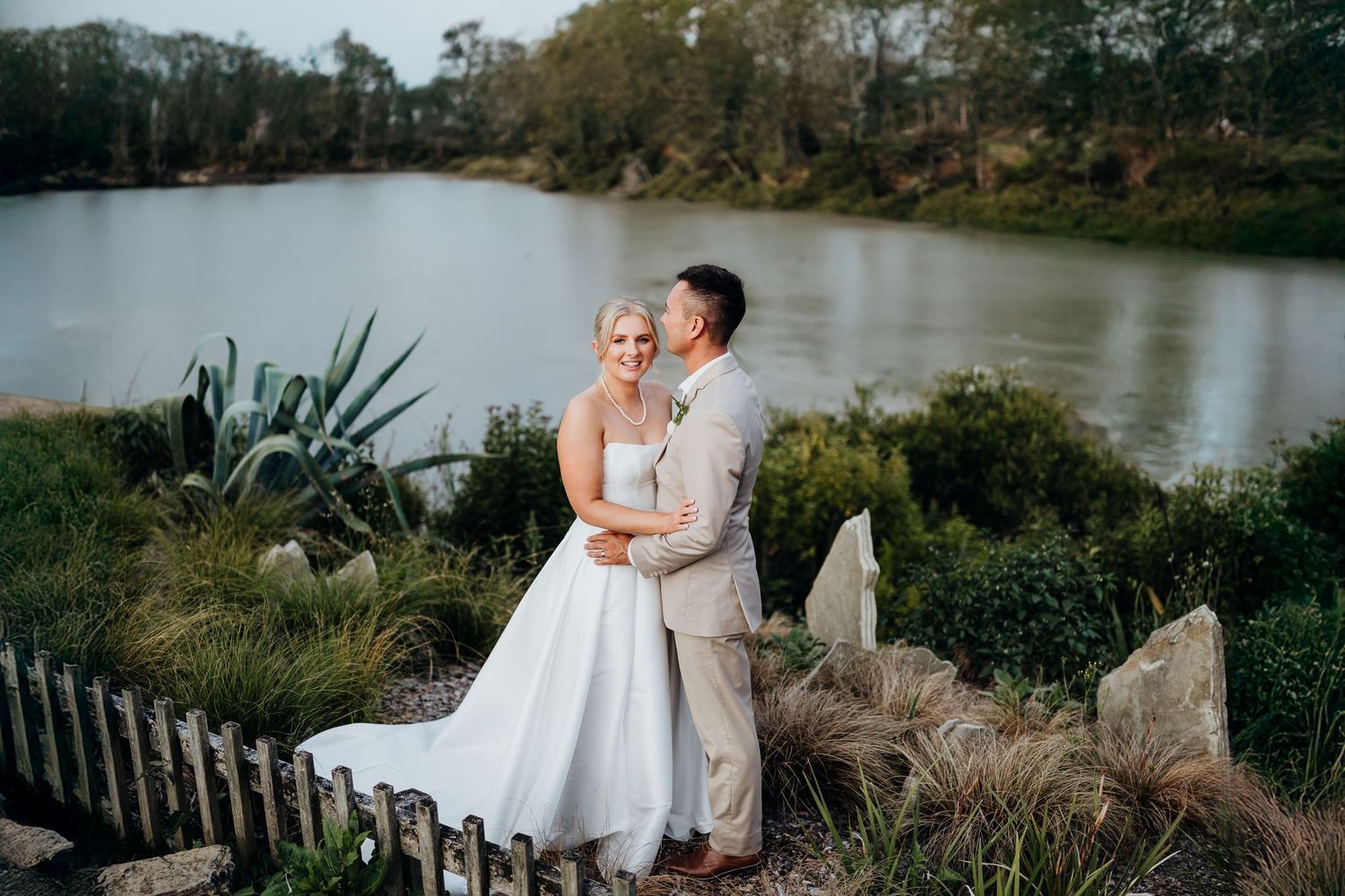 A couple shares a romantic moment on a dock overlooking a serene lake surrounded by trees.