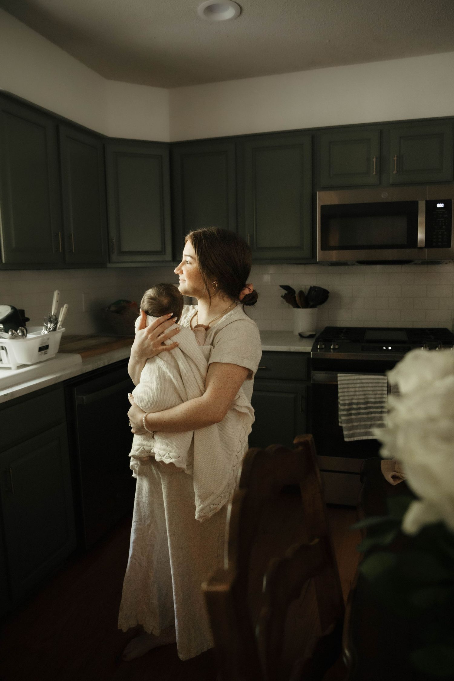 A parent holding a baby while standing in a modern kitchen with dark cabinets.