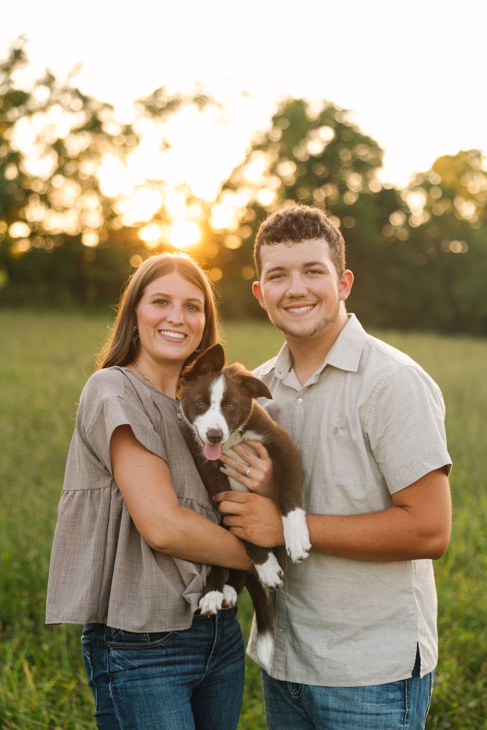 A couple poses with their adorable Basset Hound puppy in a sun-drenched field during golden hour.