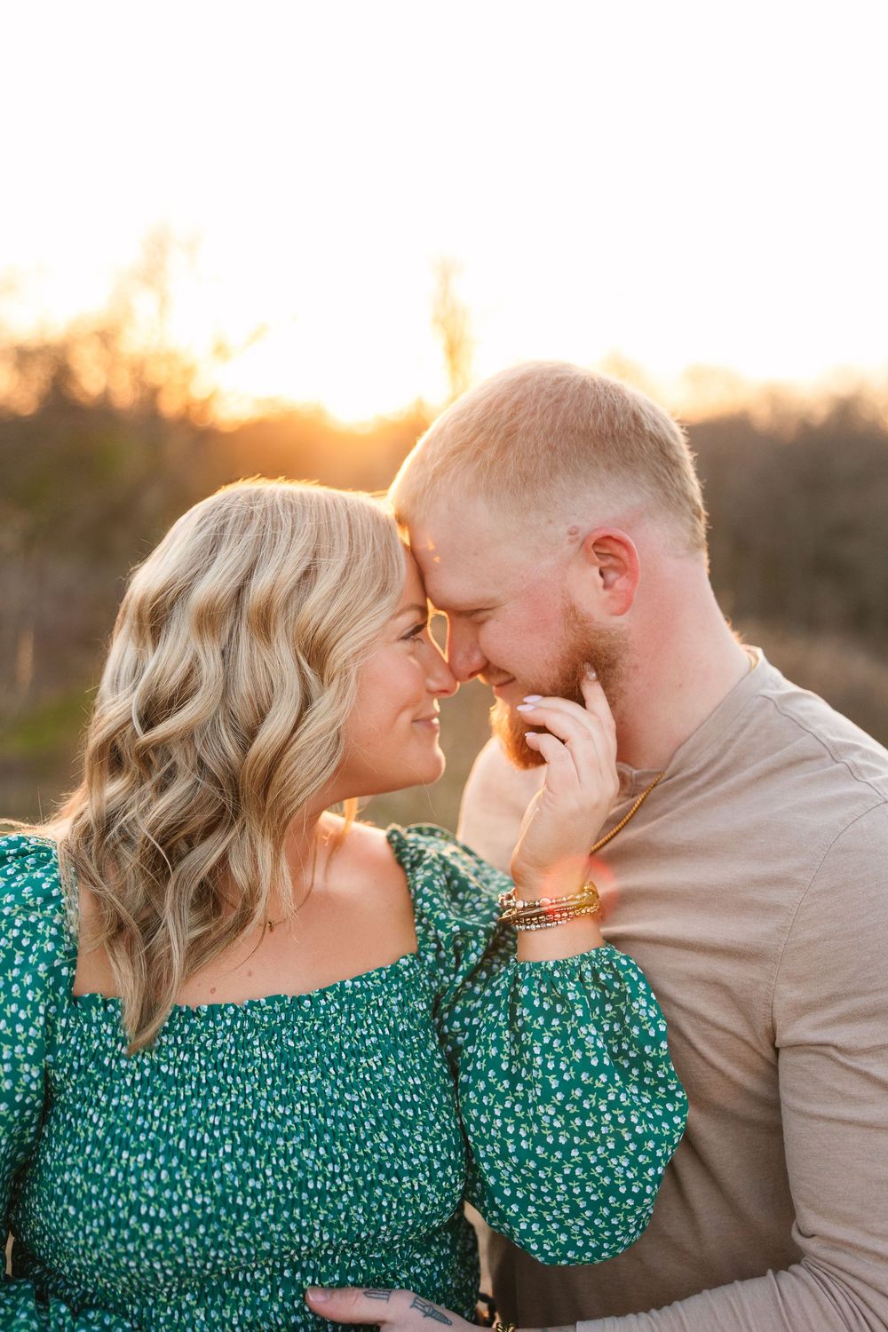 A romantic couple shares an intimate moment at sunset, with her wearing a green floral dress against a golden sky.