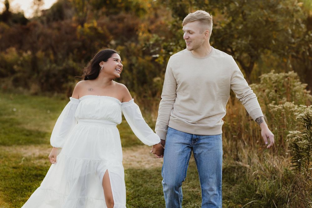 Couple holding hands and laughing together in a sunny field during engagement photos.