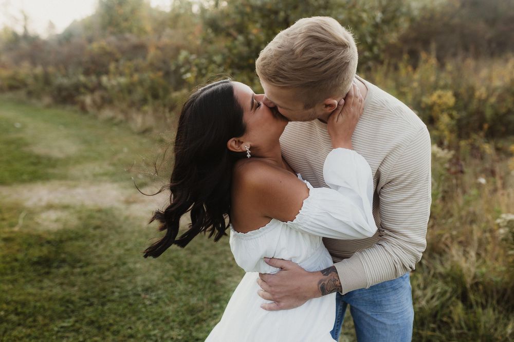 Romantic moment between couple embracing outdoors in white dress and cream sweater.