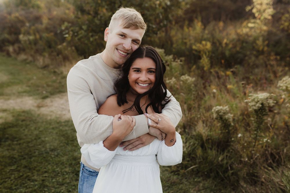Happy couple embracing and smiling at camera during outdoor engagement photo session.