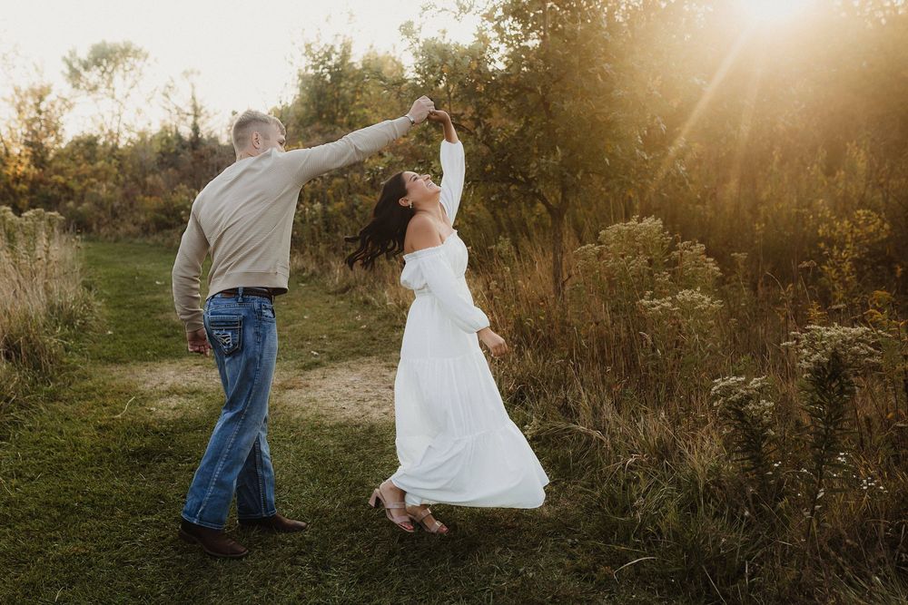 Couple dancing in golden sunset light on outdoor path surrounded by autumn foliage.