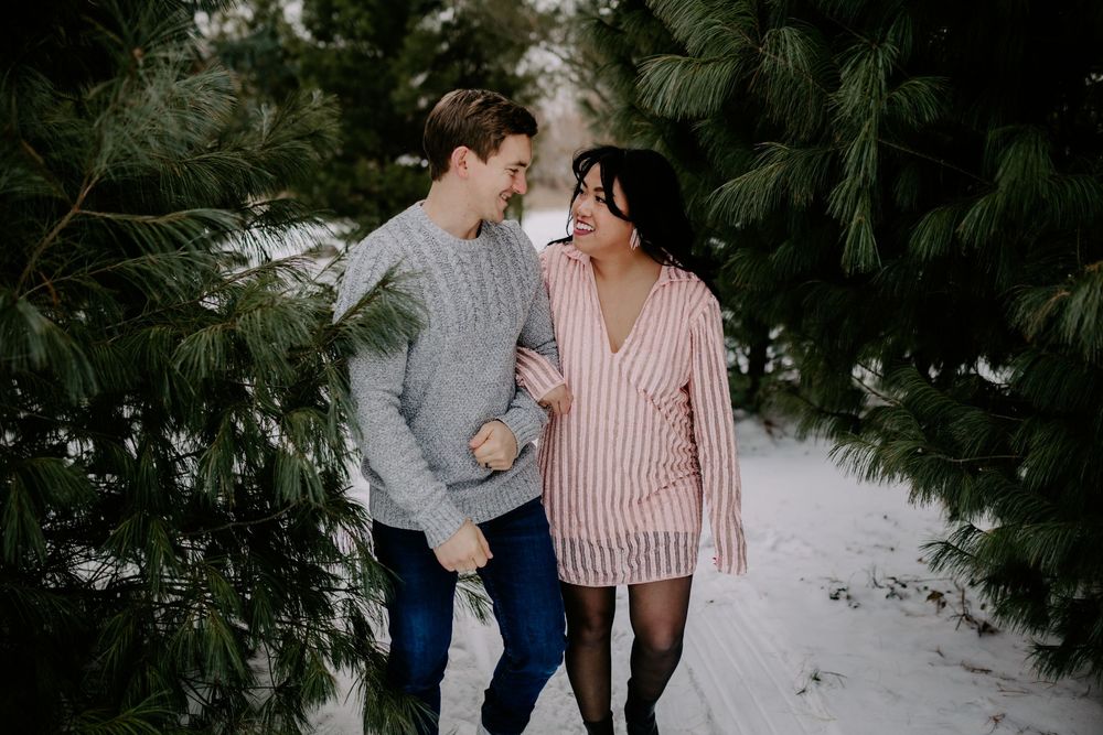 A cozy couple laughs together wearing matching sweaters in a snowy outdoor setting.